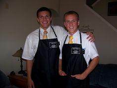 two men in black aprons standing next to each other with their arms around each other