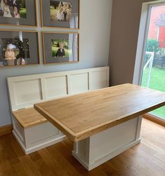 a wooden table sitting in the middle of a room with pictures on the wall behind it