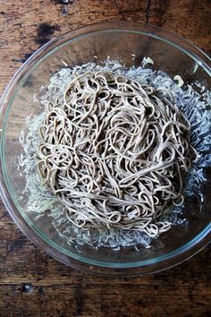 a glass bowl filled with noodles on top of a wooden table