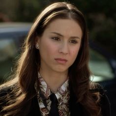 a woman with long brown hair wearing a black jacket and neck tie in front of a car