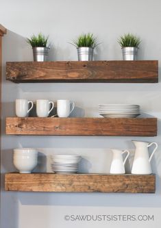 three wooden shelves with white dishes and cups on them, along with two potted plants