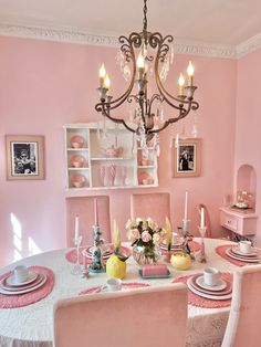 a dining room with pink walls and white table cloths on the table, chandelier in the background