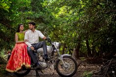 a man and woman sitting on a motorcycle in the middle of some trees, posing for a photo