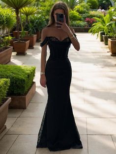 a woman in a black dress taking a selfie with her cell phone while standing outside