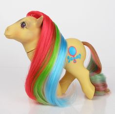 a toy pony with multi - colored hair is standing on a white surface