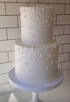 a three tiered white wedding cake sitting on top of a table next to a brick wall