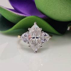 an engagement ring with three pear shaped diamonds on it and purple flowers in the background