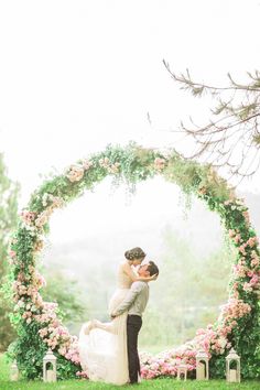 a bride and groom kissing in front of a floral arch