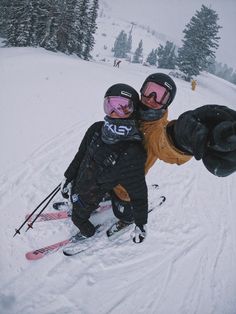 two people standing on skis in the snow with their arms around each other's shoulders