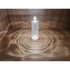 a glass candle is sitting on a wooden surface with the light reflecting off it's side