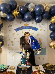 a woman standing in front of a blue and gold cake