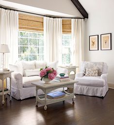 a living room filled with white furniture and flowers in vases on the coffee table