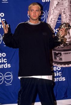 a man standing in front of a blue backdrop holding a trophy and wearing black pants