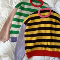 three sweaters are laying on top of each other and one has a pink ring