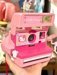 a pink polaroid camera with hello kitty on the front is held up by a hand