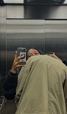 a woman taking a selfie with her cell phone in front of a stainless steel wall