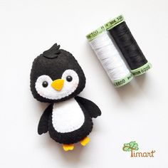 a small black and white penguin next to a spool of thread