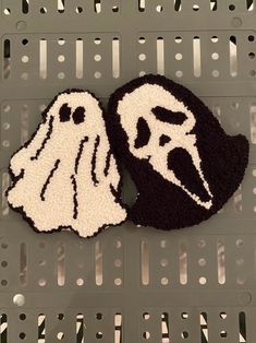 two black and white knitted ghost masks sitting on top of a metal grate