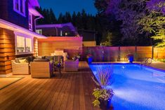 a backyard with a swimming pool and decking area at night, lit up by blue lights