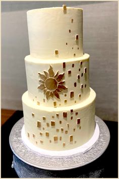 a three tiered white cake with gold designs on it's sides and the top layer is square