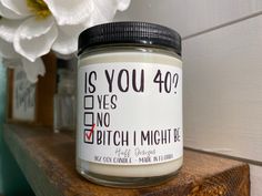 a jar of white candles sitting on top of a wooden shelf next to a flower