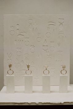 three white pedestals with rings on them in front of a large piece of artwork