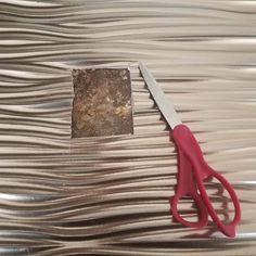 a pair of red scissors sitting on top of a piece of silver foil next to a square