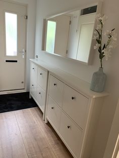 a white dresser sitting next to a door with a vase on it's side