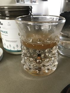 a glass vase sitting on top of a counter next to a jar of food and a spoon