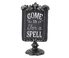 a black and white sign that says, come in for a spell on it's stand