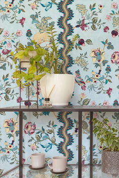 a table with two cups and a vase on it next to a wallpapered wall