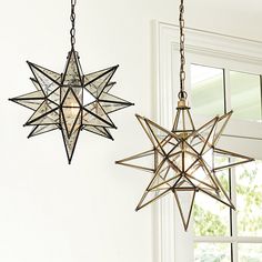 two star shaped lights hanging from the ceiling in a room with white walls and windows