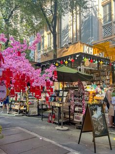 people are shopping at an outdoor market with pink flowers in the foreground and onlookers