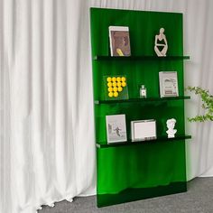 a green book shelf with pictures and other items on it next to a white curtain