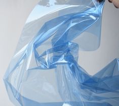 a person holding a blue plastic bag over a white wall with an object in the background