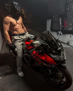 a shirtless man standing next to a red motorcycle