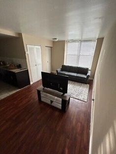 an empty living room with hard wood flooring and black leather couch in the corner