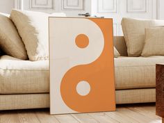 an orange and white painting sitting on top of a wooden floor next to a couch