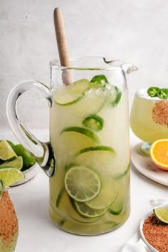 a pitcher filled with lemonade and limes next to two plates of food on a table