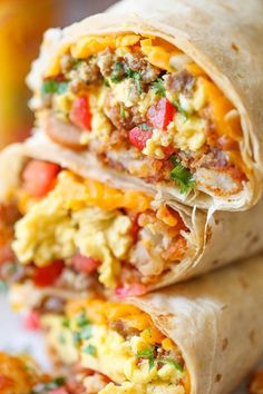 breakfast burritos stacked on top of each other with eggs, tomatoes and cheese