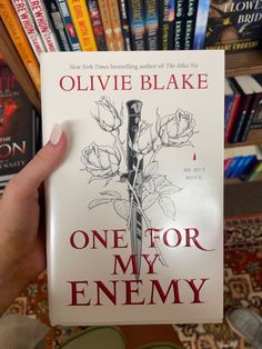 a person holding up a book in front of a bookshelf