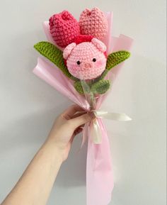 a hand holding a pink crocheted flower with two little pigs on it's head