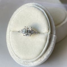 an engagement ring sits in a white velvet box on top of a cloth covered cushion