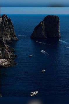 several boats are in the water near some large rocks and cliffs, with one boat on it's side