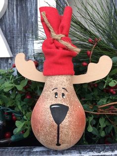 a ceramic reindeer head with a red scarf on it's head and nose is sitting in front of some evergreens