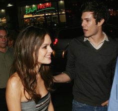 a man and woman standing next to each other in front of a building at night