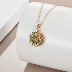 a gold necklace with a sunflower pendant on it's chain, sitting on a white surface