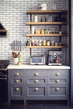 a kitchen with white brick walls and gray cabinets, an oven, microwave, toaster and coffee maker