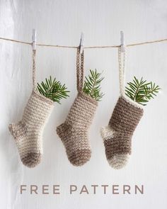 three crocheted christmas stockings hanging on a clothes line with pine branches in them