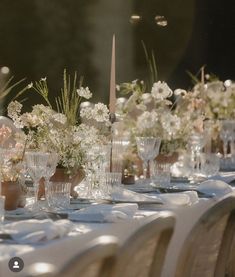 a long table is set with white flowers and vases on it for a formal dinner